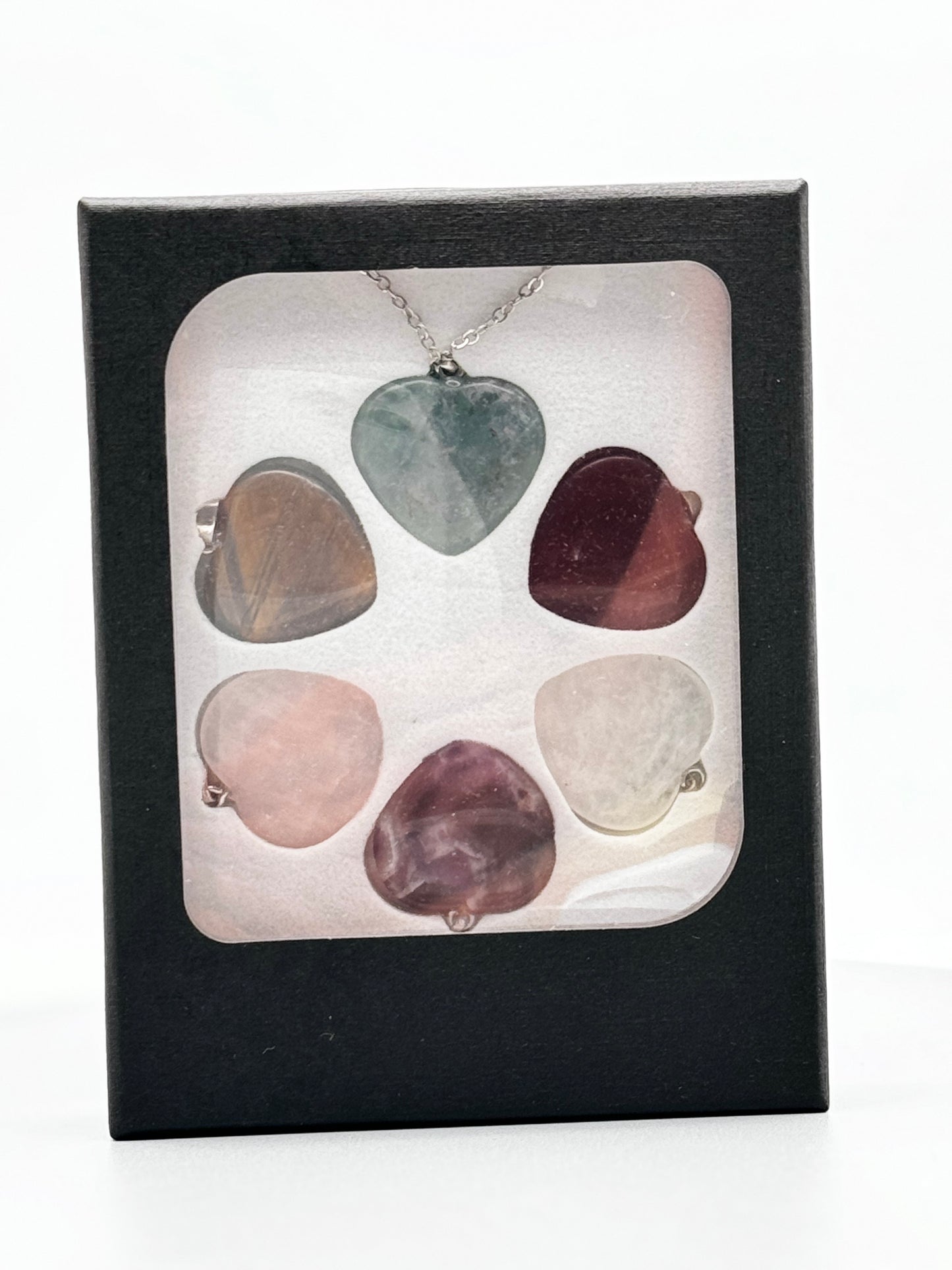 Silberne Kette mit sechs Herz-Anhängern, die mit austauschbaren Kristallen wie Rosenquarz und rotem Jaspis positive Energie verleihen.